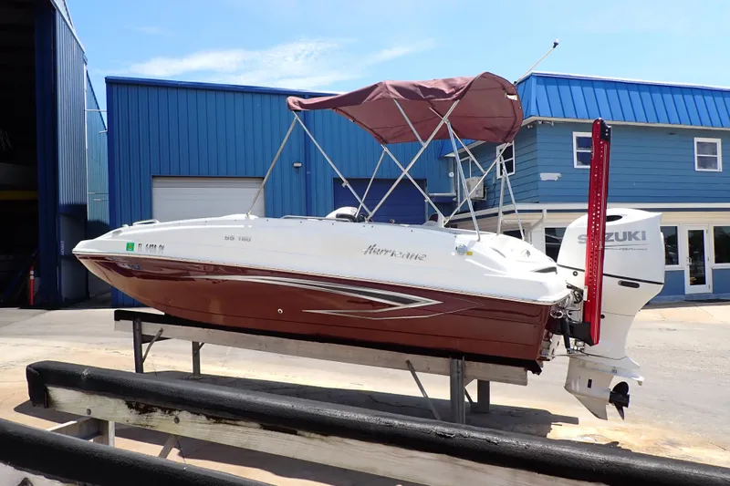 Slide: The Image of 2021 Hurricane SunDeck Sport 185 OB boat with Suzuki outboard motor, docked near blue building. - 1