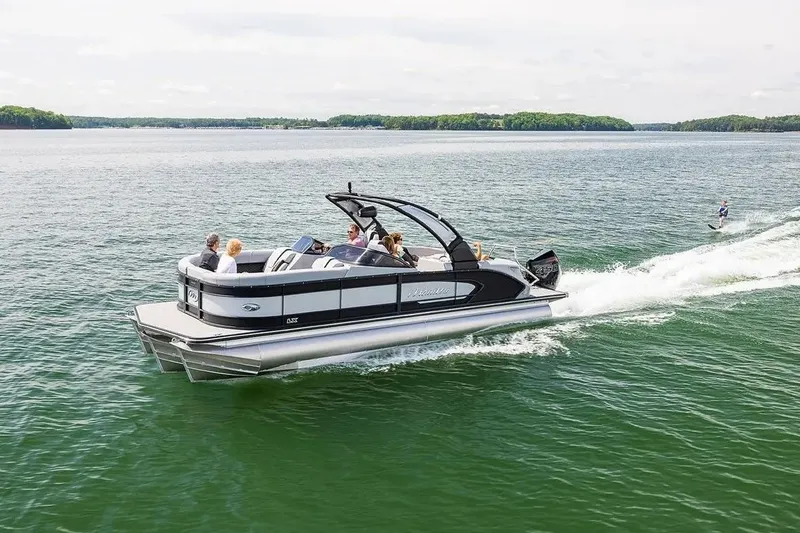 The Image of 2023 Manitou 25 LX RFXW pontoon boat cruising on a lake with passengers. - 1