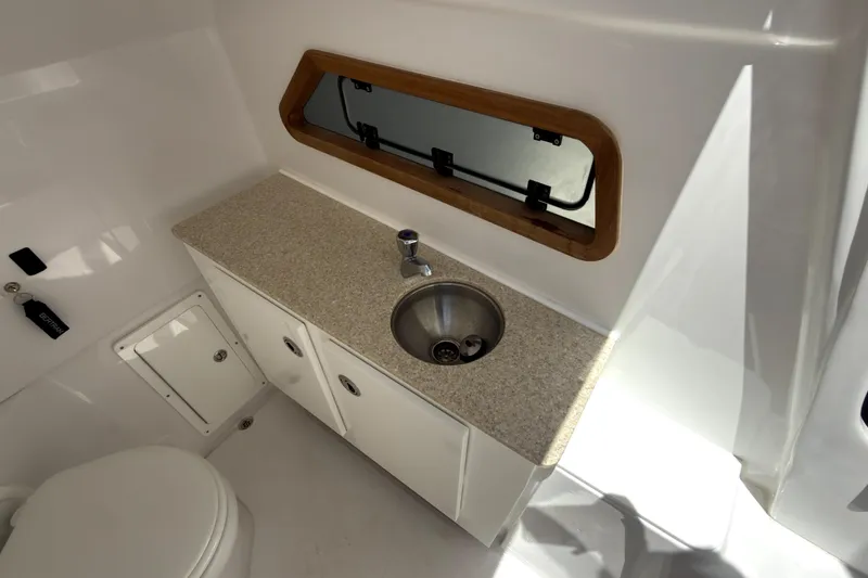 Slide: The Image of Interior of 2023 Bertram 28 CC boat featuring a compact bathroom with sink and window. - 13