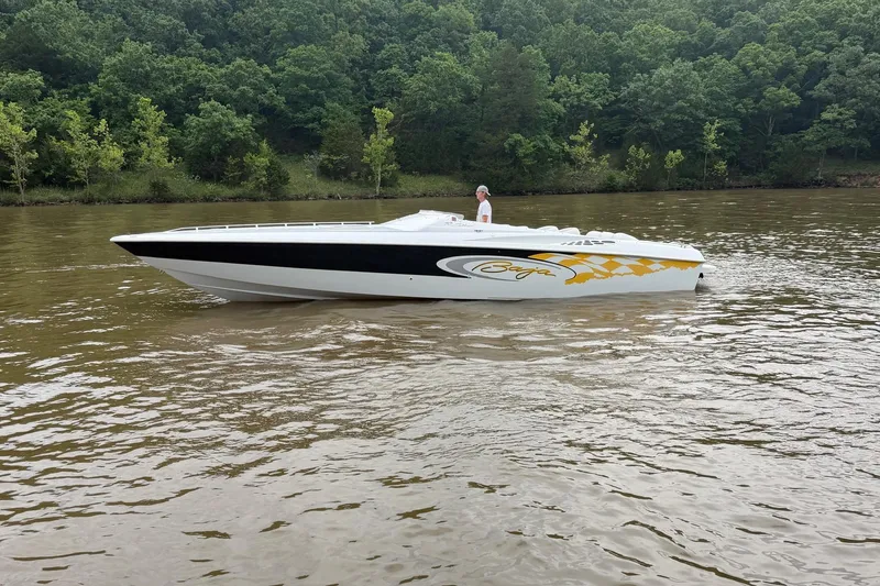 The Image of 2001 Baja 33 Outlaw speedboat cruising on a calm river with lush green forest backdrop. - 0