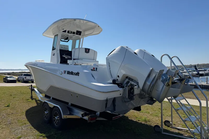 Slide: The Image of 2026 Wellcraft 243 Fisherman boat on trailer, dual outboard engines, parked near marina. - 2