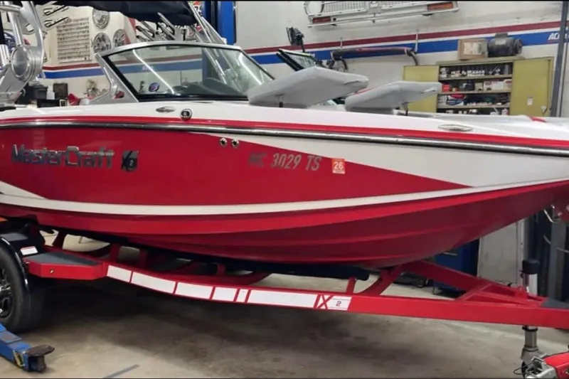 The Image of 2014 MasterCraft X-2 boat in a garage, red and white design on trailer. - 7