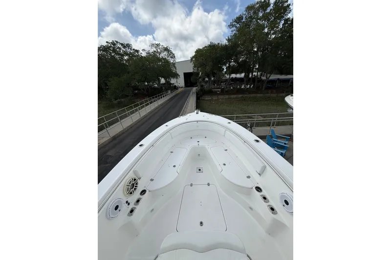 Slide: The Image of 2018 Edgewater 320CC boat deck with seating, docked near a tree-lined path under cloudy skies. - 7