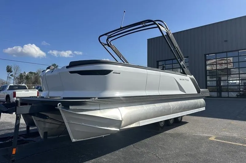 Slide: The Image of 2024 Manitou Cruise 22 Max Bench V-Toon pontoon boat on trailer, outdoor setting. - 4