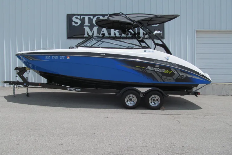 The Image of 2017 Yamaha Boats 242X E-Series in blue, parked on a trailer outside a marine shop. - 0