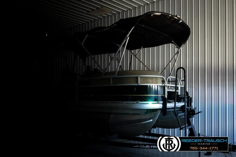 Slide: The Image of 2022 SUNTRACKER BASS BUGGY 18 DLX pontoon boat in a dimly lit storage facility. - 4