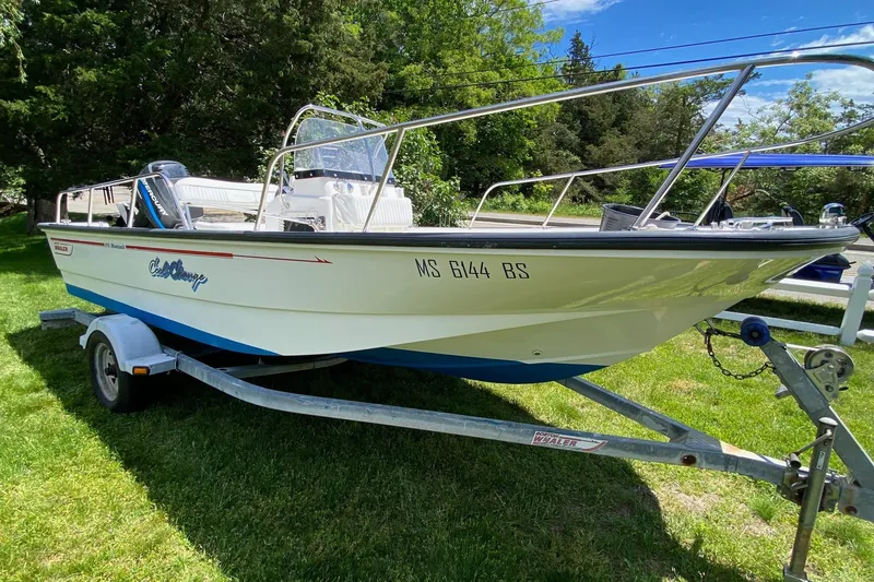 The Image of 2004 Boston Whaler 170 Montauk boat on trailer, parked on grass with trees in background. - 0