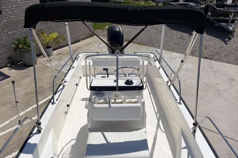 Slide: The Image of 2012 Boston Whaler 170 Montauk boat with canopy, steering console, and seating, parked on concrete. - 12