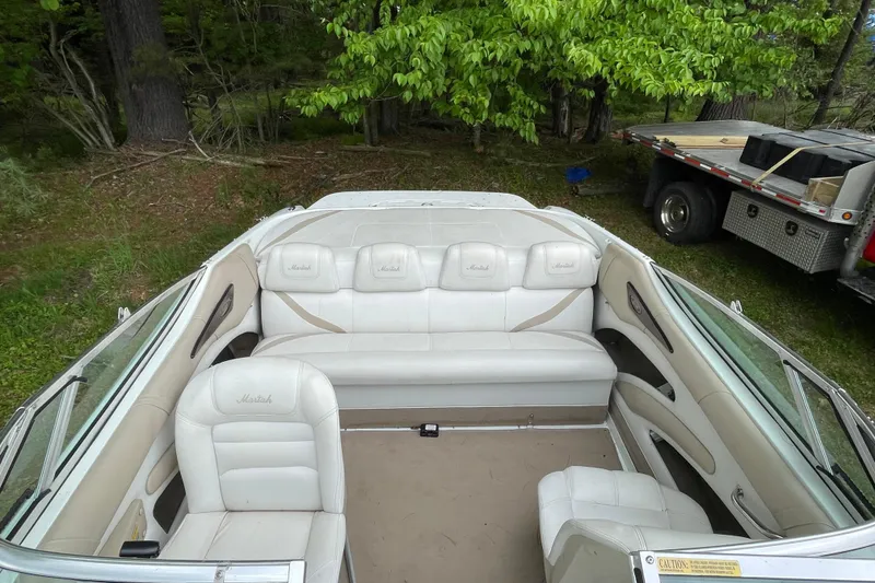 Slide: The Image of 2000 Mariah 202 Shabah boat interior with white seating, parked near trees. - 7
