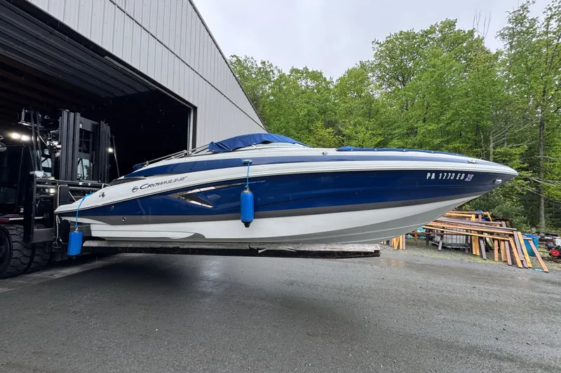 Slide: The Image of 2022 Crownline Eclipse E255 boat on forklift near warehouse, surrounded by trees. - 17