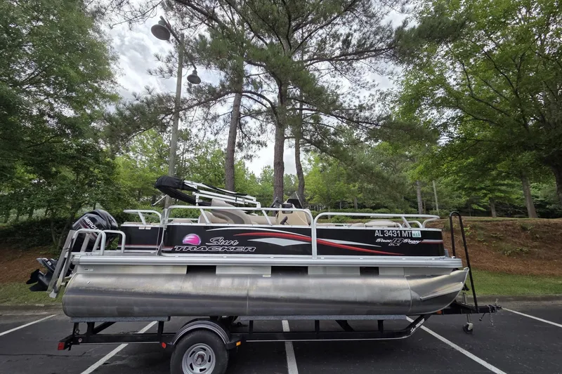 The Image of 2015 Sun Tracker Bass Buggy 18 DLX pontoon boat on trailer, parked in wooded area. - 1