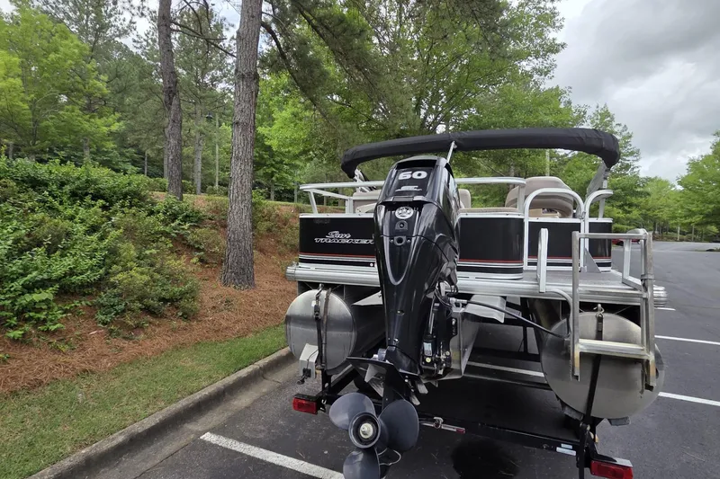 Slide: The Image of 2015 Sun Tracker Bass Buggy 18 DLX pontoon boat with outboard motor in a wooded parking area. - 4