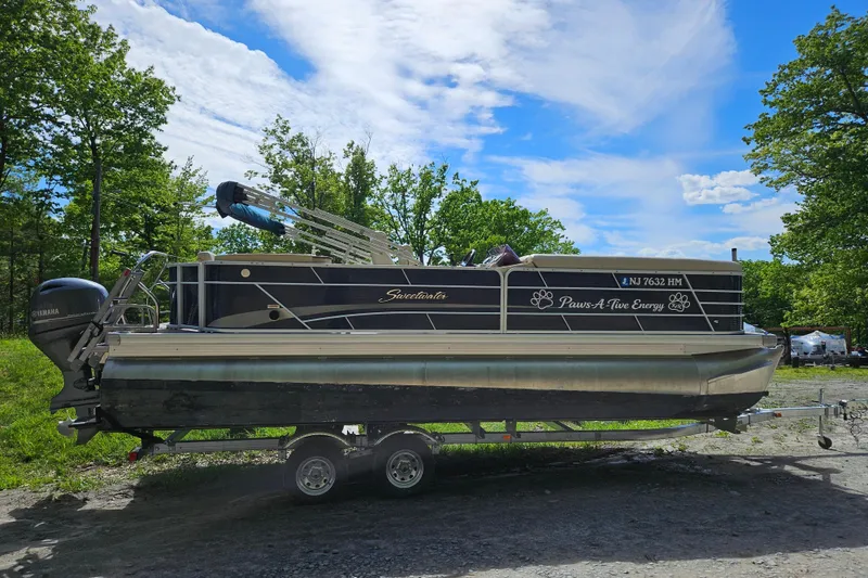 Slide: The Image of 2019 Sweetwater 2086 pontoon boat on trailer, surrounded by lush greenery and blue sky. - 5