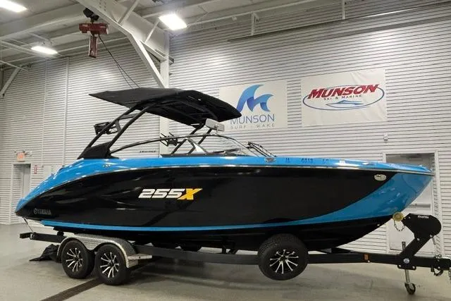 The Image of 2023 Yamaha Boats 255XE in showroom, black and blue design, on trailer. - 1