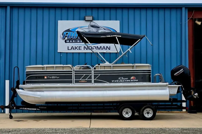 The Image of 2023 Sun Tracker Party Barge 20 DLX pontoon boat on trailer, blue building background. - 0