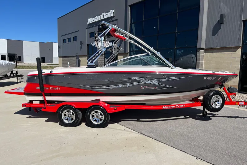 Slide: The Image of 2007 MasterCraft X-15 boat on red trailer, parked outside modern building. - 2