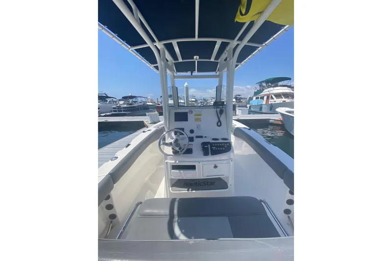 Slide: The Image of 2023 NauticStar 242L Offshore boat interior at marina, featuring steering console and seating. - 12