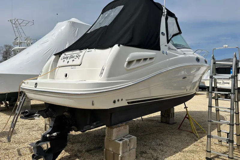 Slide: The Image of 2008 Sea Ray Sundancer 260 boat on blocks, covered, with ladder nearby. - 2