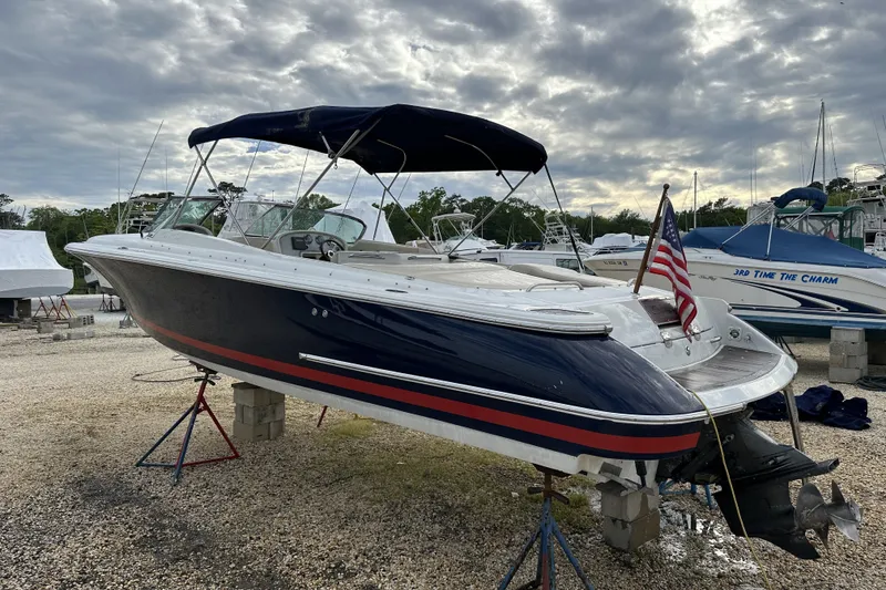 The Image of 2005 Chris-Craft Launch 28 boat on stands, with American flag, under cloudy sky. - 0
