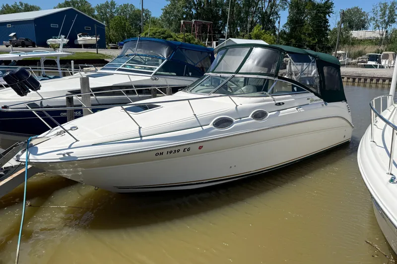 The Image of 2002 Sea Ray Sundancer 260 docked at marina, featuring sleek white design and green canopy. - 0
