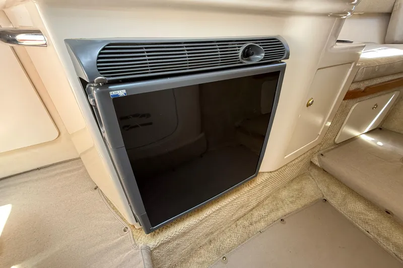 Slide: The Image of 2002 Sea Ray Sundancer 260 cabin interior with compact refrigerator and beige carpeting. - 28