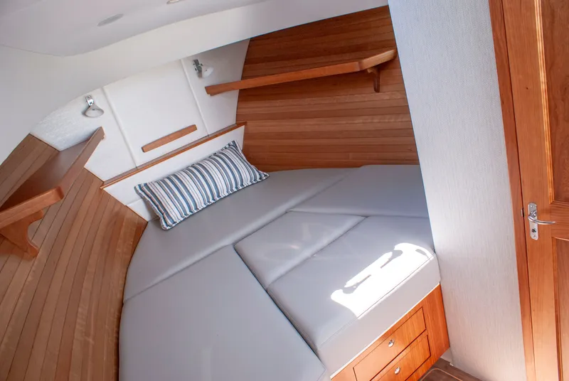Slide: The Image of MJM Yachts 38R 2027: Cozy cabin with wood paneling, gray cushioned bed, and striped pillow. - 38