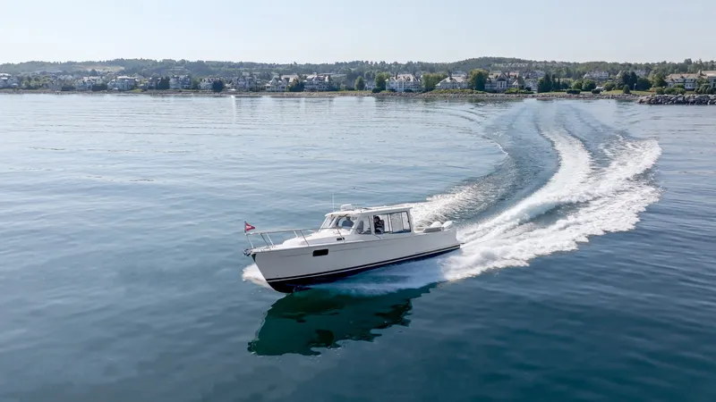 Slide: The Image of A sleek 2027 MJM Yachts 38R boat cruising on calm waters with a cityscape in the background. - 2