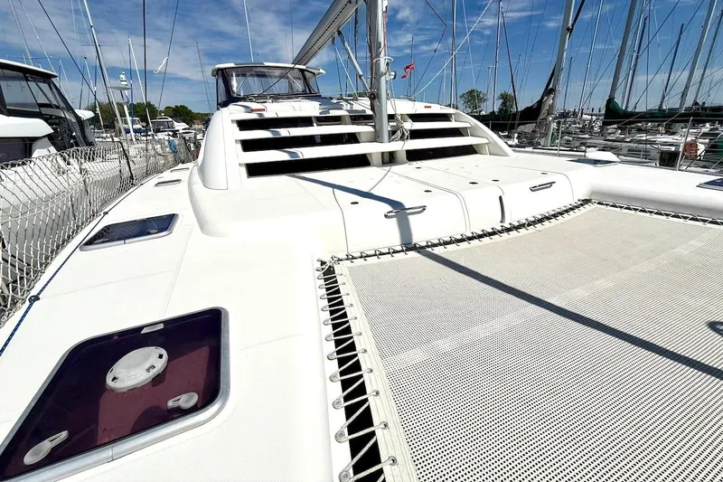 Slide: The Image of 2010 Leopard 46 catamaran docked, featuring spacious deck and netting under clear skies. - 12