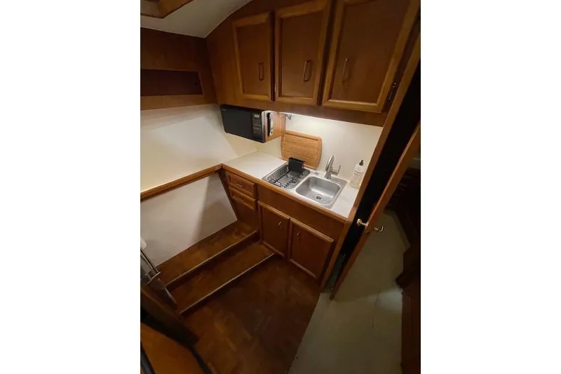 Slide: The Image of Compact kitchen area in a 1984 Egg Harbor 33 Convertible boat, featuring wooden cabinets and a sink. - 31