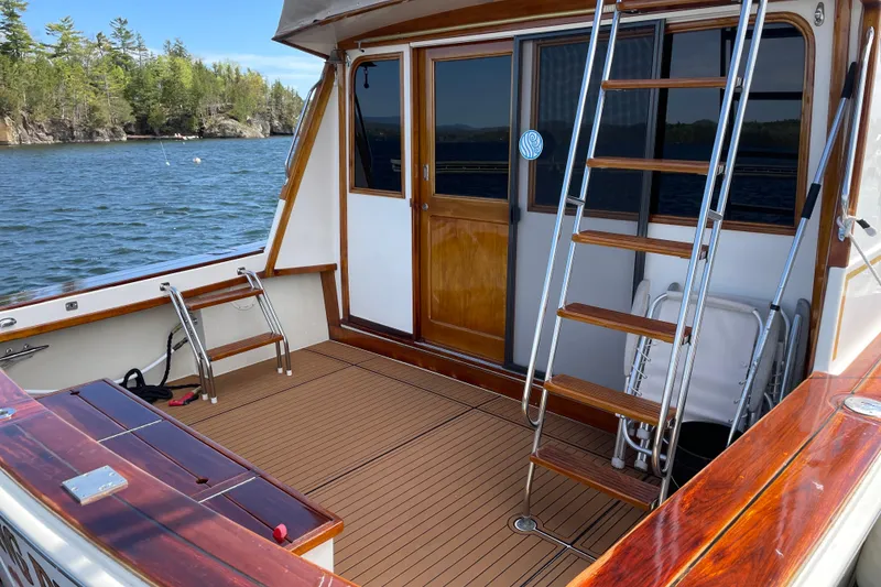 Slide: The Image of 1984 Egg Harbor 33 Convertible boat deck with wooden flooring and ladder, docked by a scenic lake. - 4