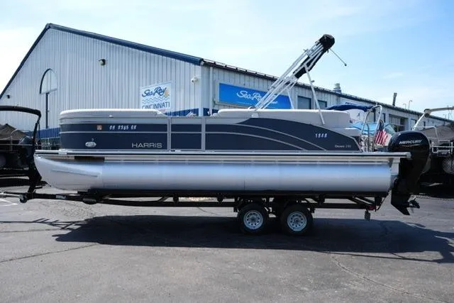 The Image of 2023 Harris Cruiser 230 CW pontoon boat on trailer, parked outside a marine dealership. - 1