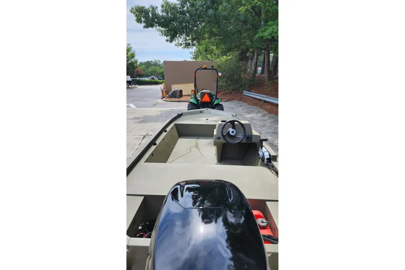 Slide: The Image of 2026 Tracker Grizzly 1648 SC boat with steering console, parked outdoors near trees. - 5