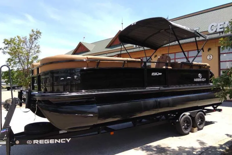 Slide: The Image of 2026 Regency 230 DL pontoon boat on trailer, parked outdoors near a building. - 66
