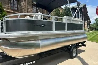Slide: The Image of 2026 Sun Tracker Bass Buggy 16 XL Select pontoon boat on trailer, parked outdoors. - 4