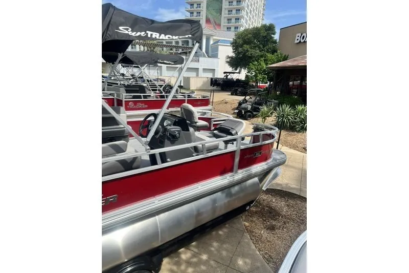 Slide: The Image of 2026 Sun Tracker Bass Buggy 16 XL Select pontoon boat with canopy, parked outdoors. - 3