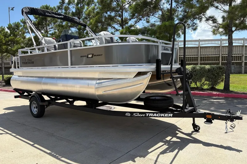 Slide: The Image of 2026 Sun Tracker Bass Buggy 18 DLX pontoon boat on trailer, parked outdoors. - 2