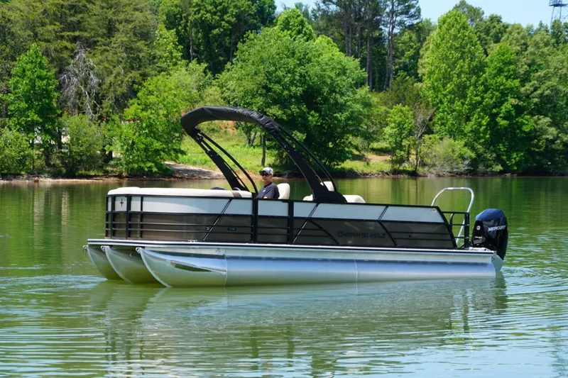 Slide: The Image of 2026 Berkshire 22 UL CTS pontoon boat cruising on a serene lake with lush green surroundings. - 2