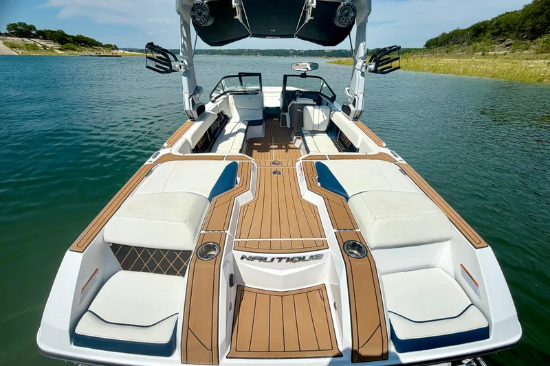 Slide: The Image of 2022 Nautique Super Air Nautique GS24 boat on a serene lake, showcasing luxurious seating and deck. - 31