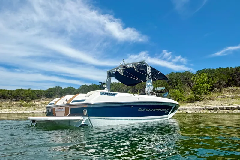 Slide: The Image of 2022 Nautique Super Air Nautique GS24 boat on a serene lake under a clear blue sky. - 8