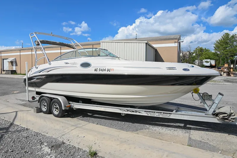 Slide: The Image of 2002 Sea Ray 240 Sundeck boat on trailer, parked outdoors under a clear blue sky. - 2