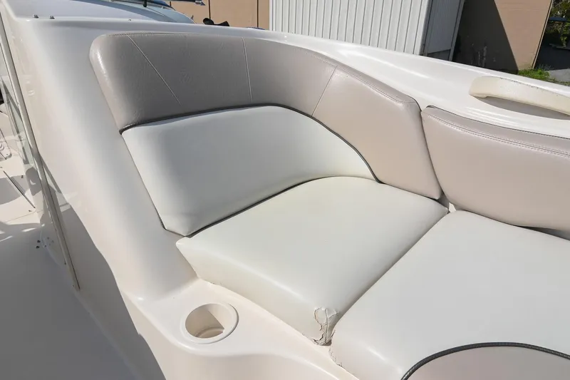 Slide: The Image of 2002 Sea Ray 240 Sundeck boat seating area with cup holder, featuring white and gray upholstery. - 23