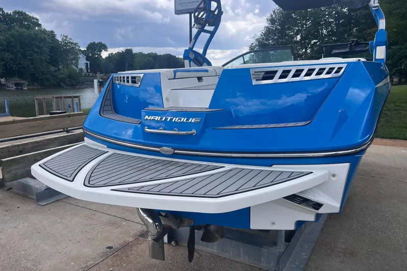 Slide: The Image of 2016 Nautique Super Air Nautique 210 boat in vibrant blue, docked by a serene lake. - 13