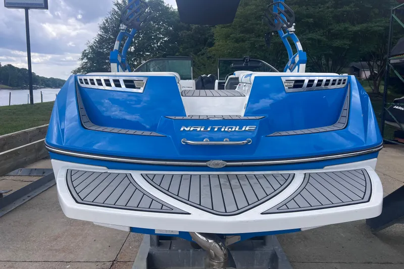 Slide: The Image of 2016 Nautique Super Air Nautique 210 boat, blue and white, docked by a lakeside. - 14