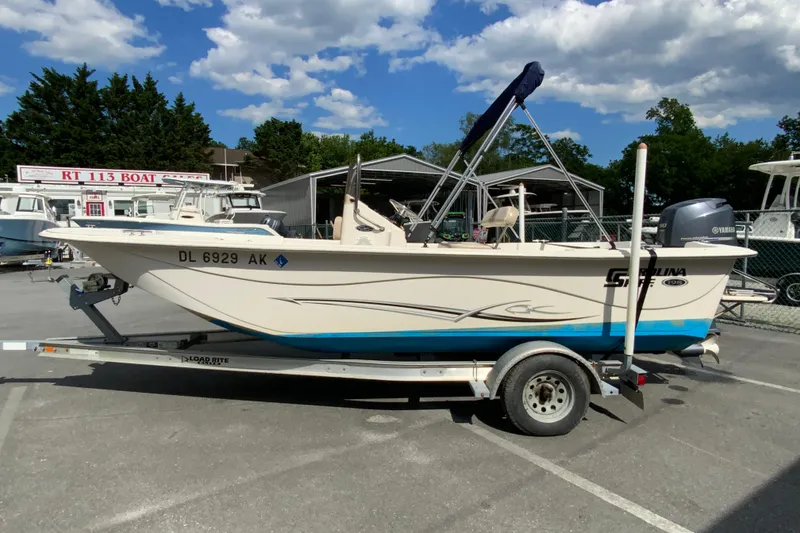 Slide: The Image of 2016 Carolina Skiff 198 DLV boat on trailer, parked outdoors under a blue sky. - 11