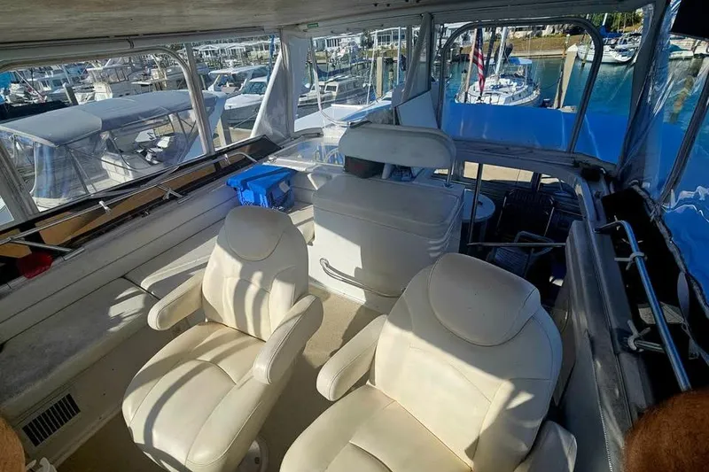 Slide: The Image of Interior view of 1998 Mainship 47 Motor Yacht with white seating and marina backdrop. - 15