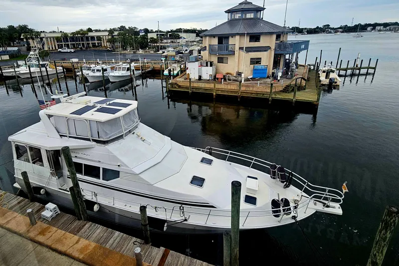Slide: The Image of 1998 Mainship 47 Motor Yacht docked at a marina with surrounding boats and buildings. - 2
