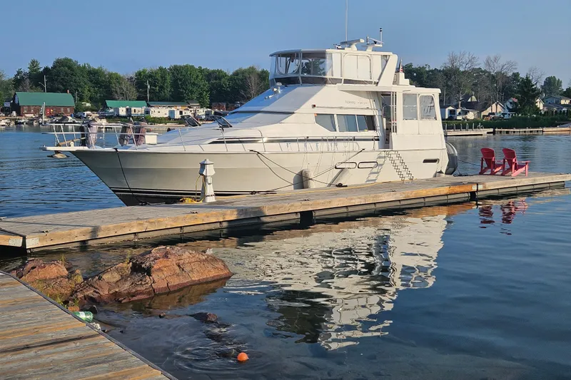 Slide: The Image of 1998 Mainship 47 Motor Yacht docked at a serene marina with red chairs on the pier. - 3