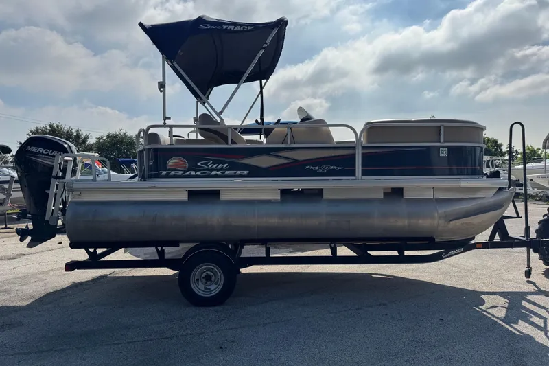 Slide: The Image of 2019 Sun Tracker Party Barge 18 DLX pontoon boat on trailer, with canopy and Mercury outboard motor. - 2