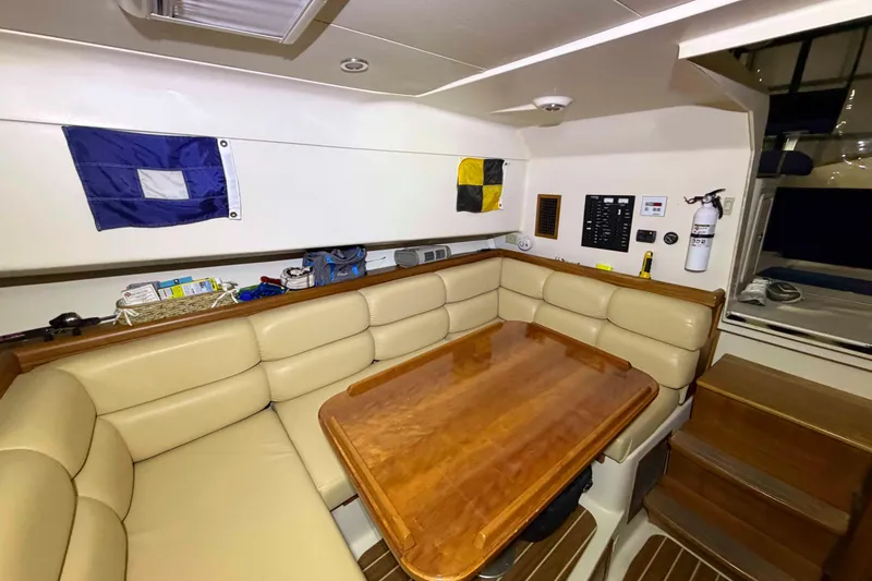 Slide: The Image of 2005 Mainship Pilot 34 interior with beige seating, wooden table, and nautical flags. - 28