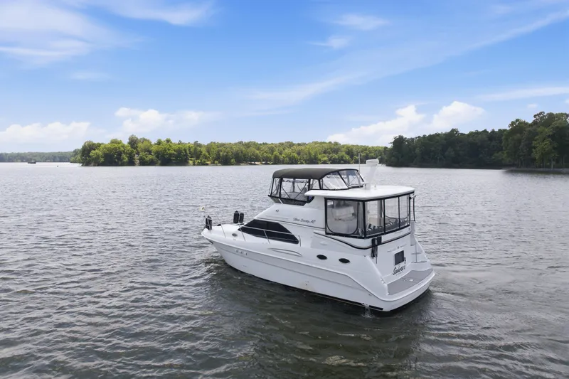 The Image of 1997 Sea Ray 370 Aft Cabin yacht cruising on a serene lake under a clear blue sky. - 4